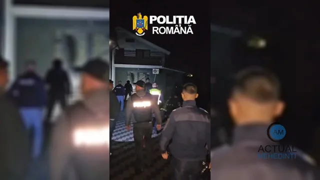 Mai mulți bărbați în uniformă întunecată stau pe un trotuar pavat lângă o clădire, în timpul nopții.