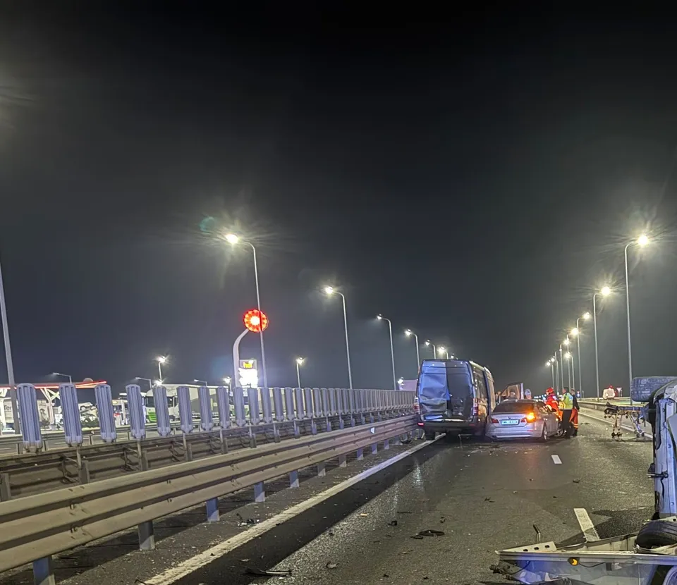Mai multe autovehicule sunt oprite pe o autostradă noaptea, lângă o barieră metalică și sub iluminat public.