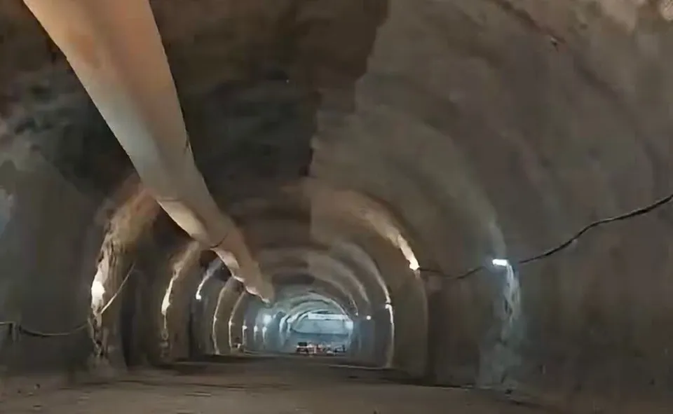 Un tunel de beton cu pereți curbați și un tub lung suspendat de tavanul acestuia se întinde spre fundul galeriei întunecate.