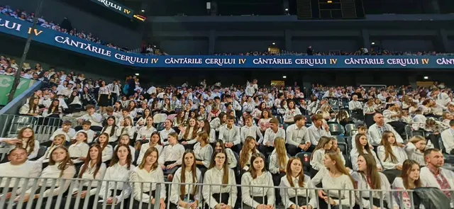 O mulțime de copii și tineri îmbrăcați în haine albe stau așezați pe scaune în tribunele unei arene închise.