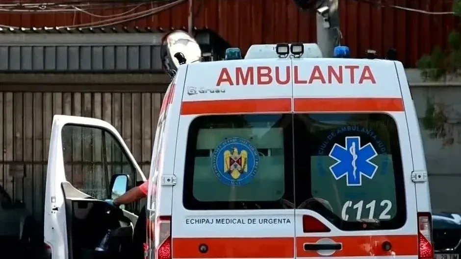 Spatele unei ambulanțe albe cu inscripții roșii și albastre, având portierele deschise și un scut de serviciu medical pe geamul din spate.