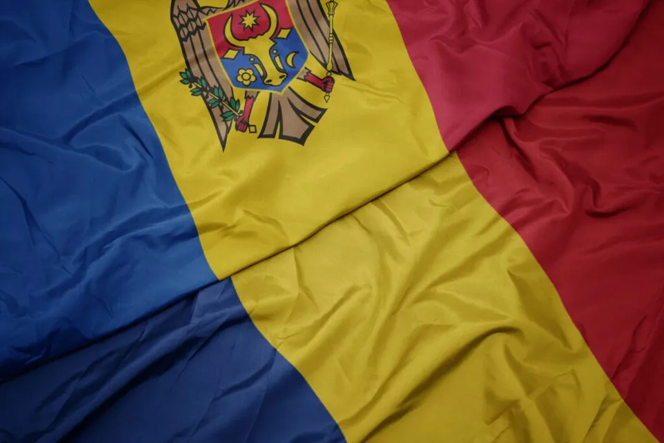 Două steaguri cu culori de albastru, galben și roșu sunt întrepătrunse și prezintă pliuri de material textil.