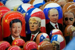 O colecție de păpuși matrăști pictate cu portretele lui Xi Jinping, Donald Trump, Vladimir Putin și alte figuri politice, pe fundalul steagelor naționale ale Chinei, SUA și Rusiei.