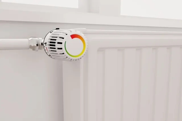 Un radiator alb este conectat la o conductă prin intermediul unui termostat cu un indicator colorat în roșu, galben și verde.
