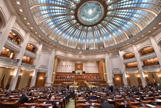 O sală circulară mare cu un dom de sticlă și o mulțime de oameni așezați la birouri în fața unui podium central.
