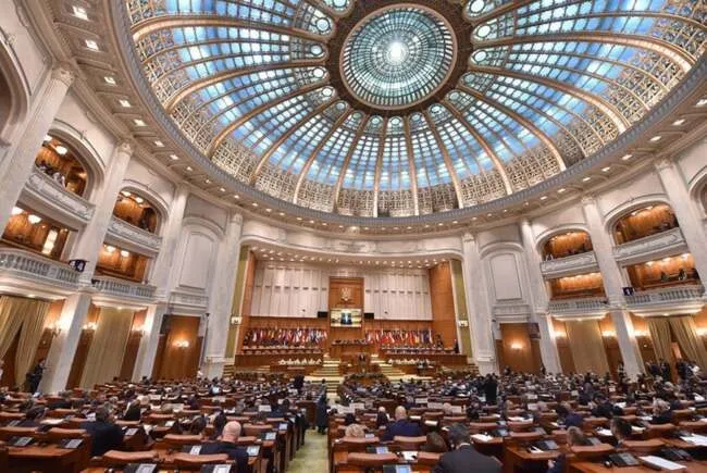 O sală circulară mare cu un dom de sticlă și o mulțime de oameni așezați la birouri în fața unui podium central.