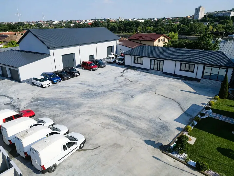 O vedere aeriană prezintă clădiri albe cu acoperișuri închise, un teren asfaltat mare și mai multe mașini parate în parcare.