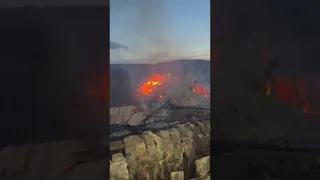 Flăcări și fum se ridică deasupra unei structuri de acoperiș într-un peisaj montan la amurg.