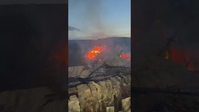 Flăcări și fum se ridică deasupra unei structuri de acoperiș într-un peisaj montan la amurg.