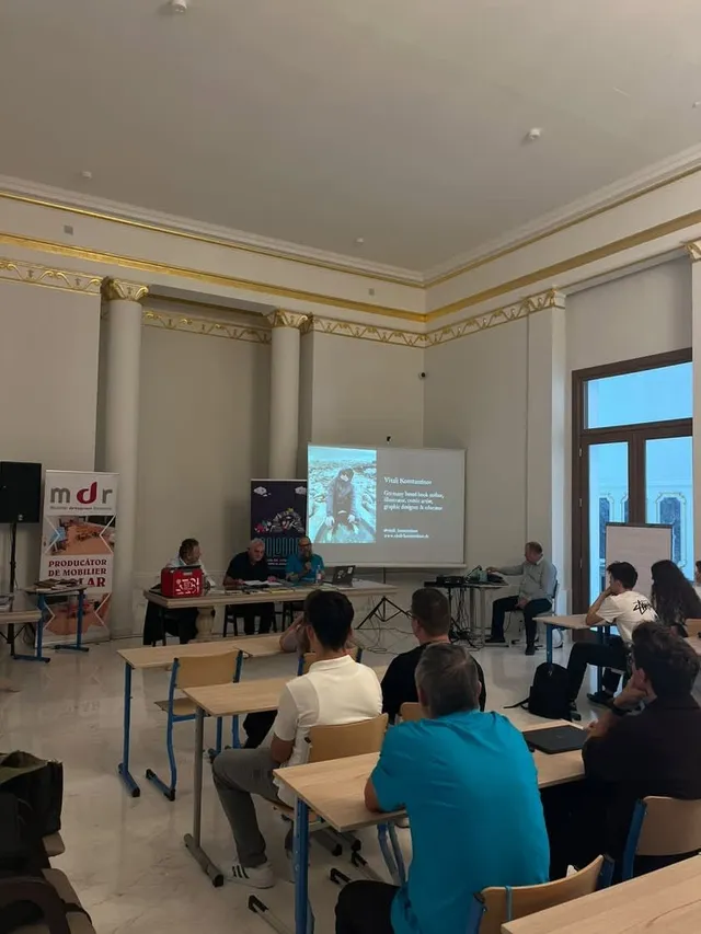 Oamenii stau la mese în fața unui ecran de proiecție care afișează un text și o imagine într-o încăpere cu coloane albe.