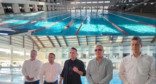 Cinci bărbați stau în rând în fața unei piscine interioare cu linii de culoare roșie și albă pe fundul apei.