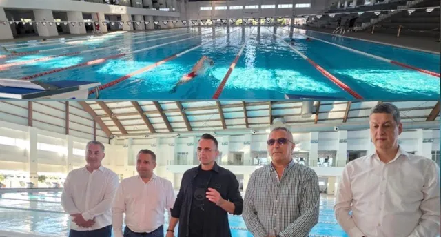 Cinci bărbați stau în rând în fața unei piscine interioare cu linii de culoare roșie și albă pe fundul apei.