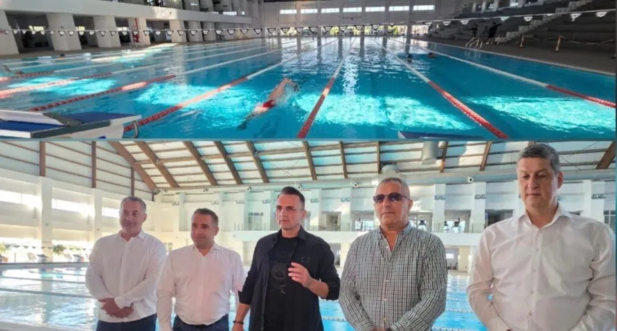Cinci bărbați stau în rând în fața unei piscine interioare cu linii de culoare roșie și albă pe fundul apei.