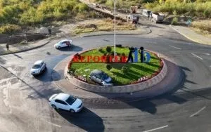 O vedere de sus a unui sens giratoriu cu mașini albe și o mașină neagră situată pe marginea insulei verzi.