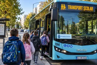 Copii cu rucsacuri urcă într-un autobuz albastru pe care scrie transport școlar.
