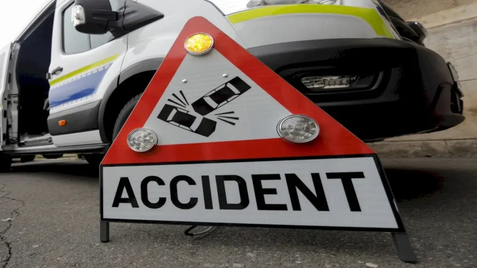 Un triunghi reflectorizant cu inscripția ACCIDENT și un simbol al unei mașini răsturnate este plasat în fața unui vehicul alb și negru.