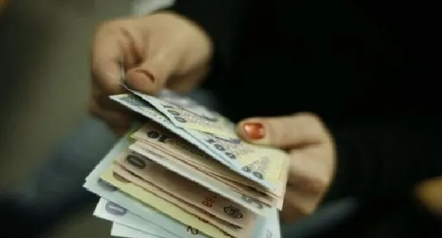 Două mâini țin un teanc de bancnote colorate cu numere imprimante pe suprafața lor.