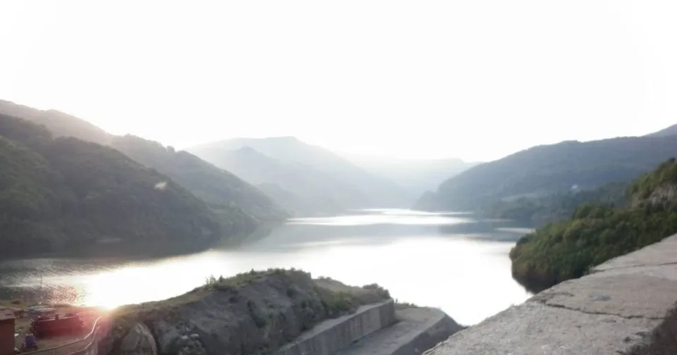 O vedere panoramică asupra unui lac înconjurat de munți sub un cer luminos.