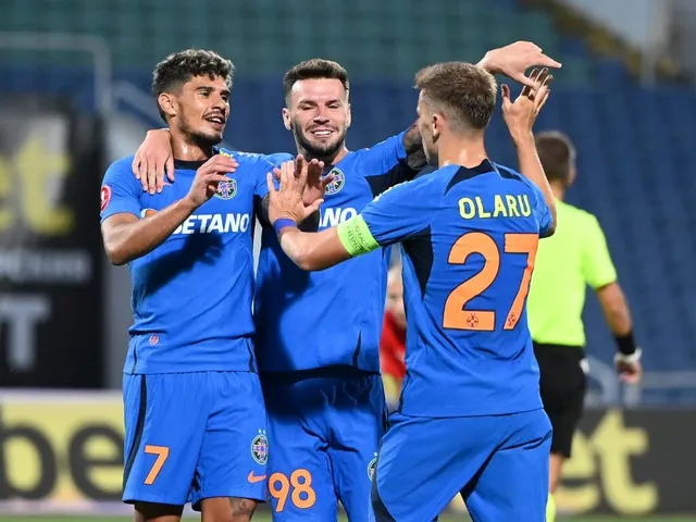 Trei jucători de fotbal în echipament albastru sărbătoresc pe un teren de fotbal, în timp ce un alt jucător în echipament galben se îndepărtează.