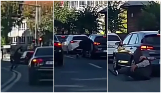 Un bărbat este așezat pe asfalt lângă un autoturism negru pe un drum urban cu alte mașini parcate în fundal.