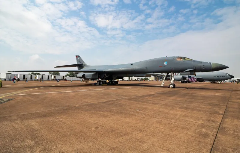 Un avion militar gri stă pe o pistă de beton sub un cer parțial înnorat, având un alt avion similar în fundal.