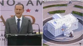 Un bărbat într-un costum gri și cravată stă în spatele unui podium, în timp ce în partea dreaptă apare o machetă a unei clădiri albe.