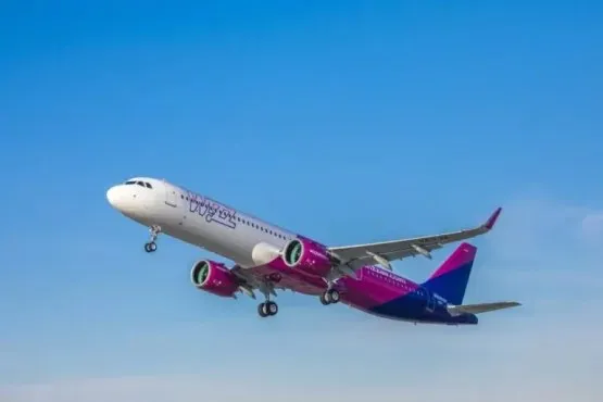 Un avion Wizz Air cu trenul de aterizare coborât zboară pe cer, într-o compoziție aeriană.