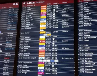 Un ecran digital afișează o listă de zboruri de plecare cu destinații, numere de zbor și orele de decolare pe un fundal negru.