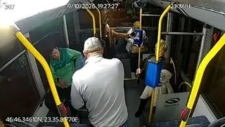 Oameni stau în interiorul unui vehicul lângă barele de prindere galbene, sub o lumină albă intensă.