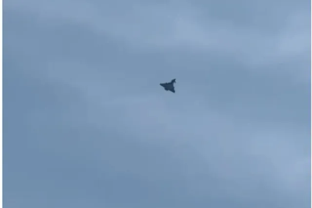 O siluetă întunecată de obiect zburător se află în centrul unui cer acoperit de nori gri.