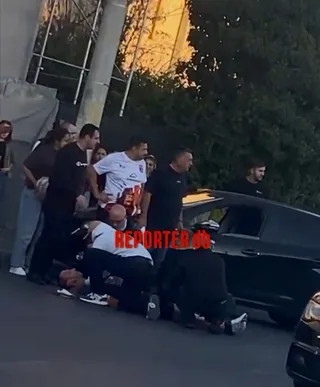 Mai mulți bărbați stau în jurul unei persoane întinse pe asfalt lângă o mașină neagră.