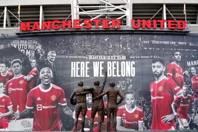 Un mural mare pe un perete exterior prezintă mai mulți fotbaliști în echipament roșu și câteva statui de bronz ale unor jucători cu spatele.