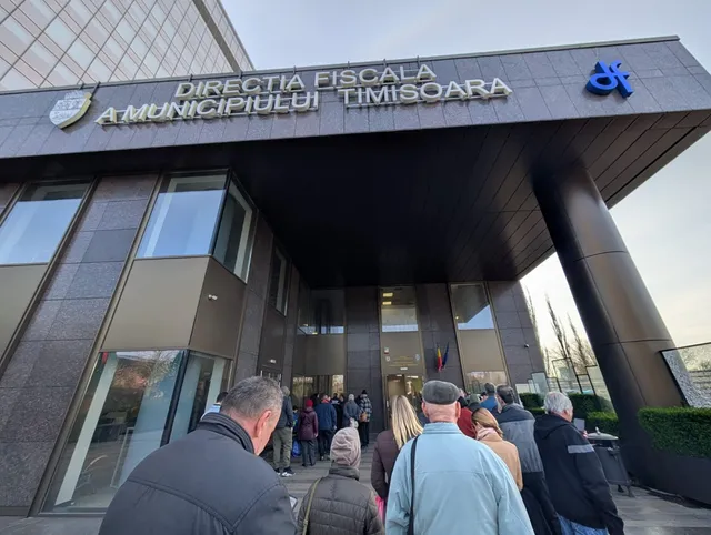 O mulțime de oameni stă la coadă în fața unei clădiri moderne cu panouri de sticlă și un panou de identificare pe fațadă.