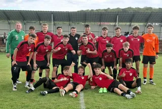 Un grup de tineri sportivi în echipamente de fotbal roșii și negre pozează pe un teren de gazon verde.