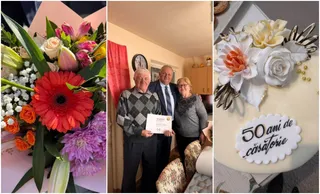Un grup de trei persoane stă în interiorul unei încăperi lângă o masă cu un tort decorat cu flori și un mesaj scris.