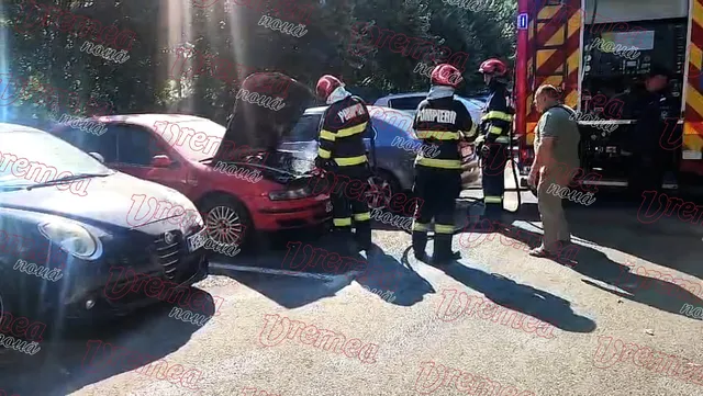 Pompieri în echipament de protecție și un bărbat stau lângă un autoturism roșu cu capota deschisă lângă un vehicul de intervenție.