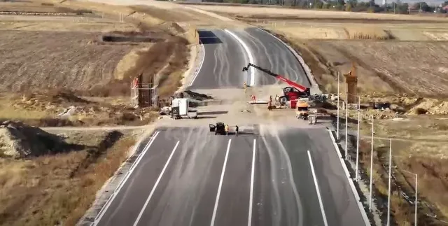 O porțiune de autostradă proaspăt asfaltată cu linii albe marcate este vizibilă lângă un utilaj cu braț telescopic roșu și terenuri excavate.