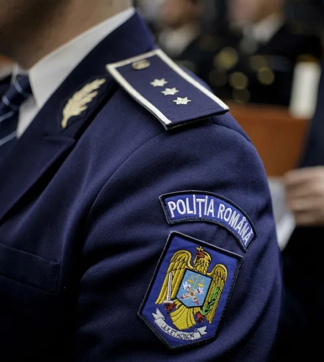 Un uniformă albastră prezintă un ecuson cu inscripția 'POLIȚIA ROMÂNĂ' și un emblema colorată pe umăr, lângă un epaulet cu trei stele.