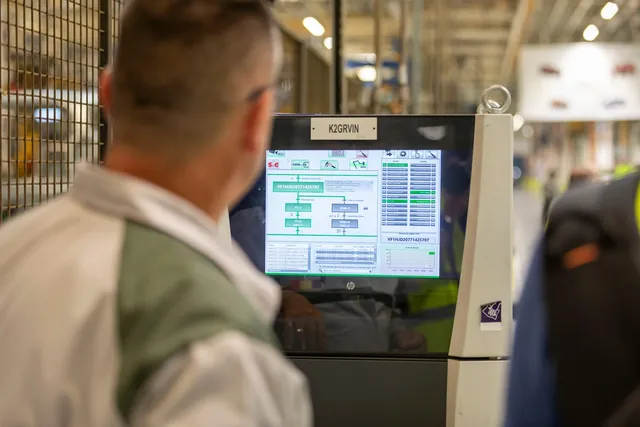 Un bărbat de spate privește un ecran digital afișând grafice și date într-un mediu industrial.