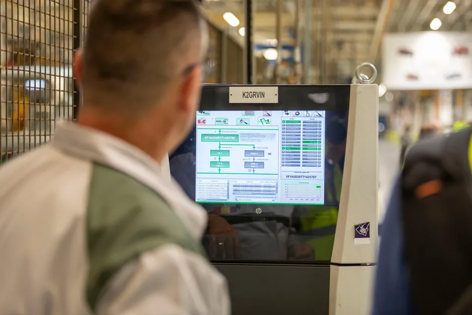 Un bărbat de spate privește un ecran digital afișând grafice și date într-un mediu industrial.