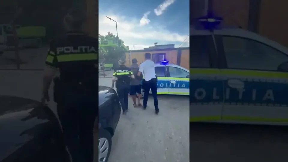 Trei persoane stau lângă o mașină de poliție albastră și albă parcată pe un drum asfaltat sub un cer înnorat.