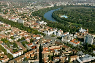 O vedere aeriană a unui oraș cu clădiri diverse, străzi și un râu care curge prin zona împădurită.