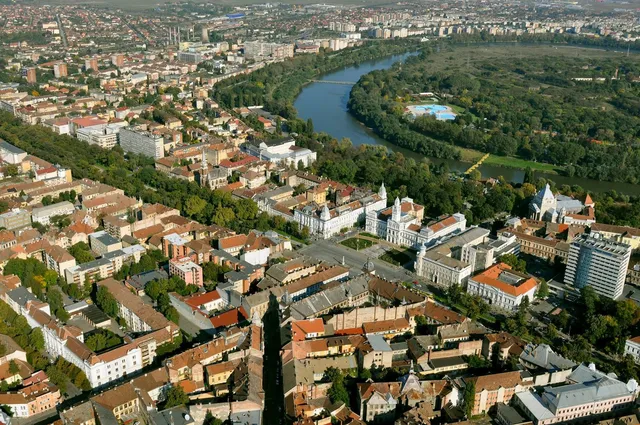 O vedere aeriană a unui oraș cu clădiri diverse, străzi și un râu care curge prin zona împădurită.