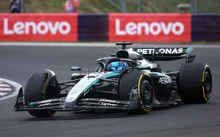 Un monopost de Formula 1 de culoare neagră și verde cu inscripții Petronas circulă pe o pistă de asfalt în fața unui panou publicitar Lenovo.