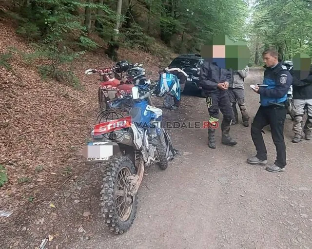 Mai multe motociclete de teren sunt parcate pe un drum de pământ lângă un vehicul negru, în prezența unor persoane îmbrăcate în haine de protecție.