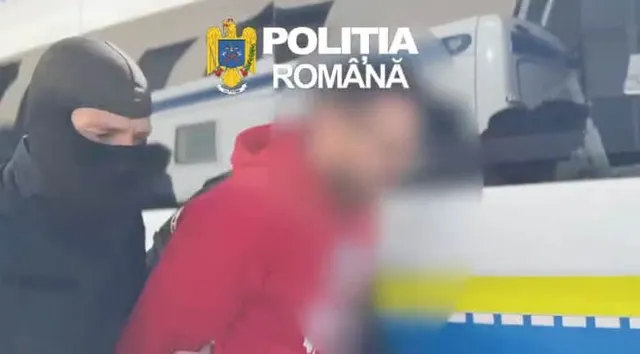 Un bărbat cu o mască neagră pe față stă lângă o persoană cu o hanorac roșie în fața unui vehicul alb.