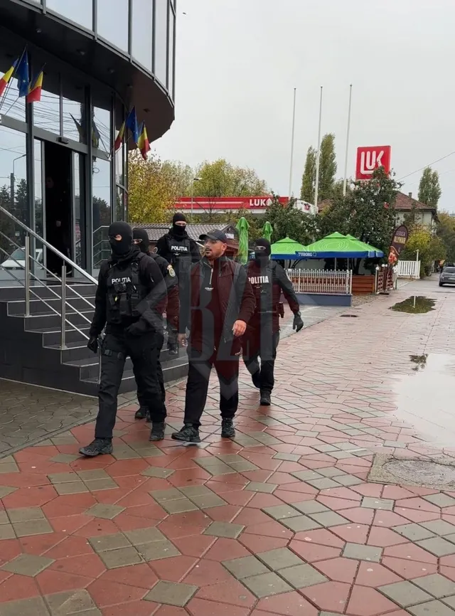 Patru persoane în uniforme negre cu inscripția POLITIA și o persoană în haine civile merg pe un trotuar din plăci roșii și gri.