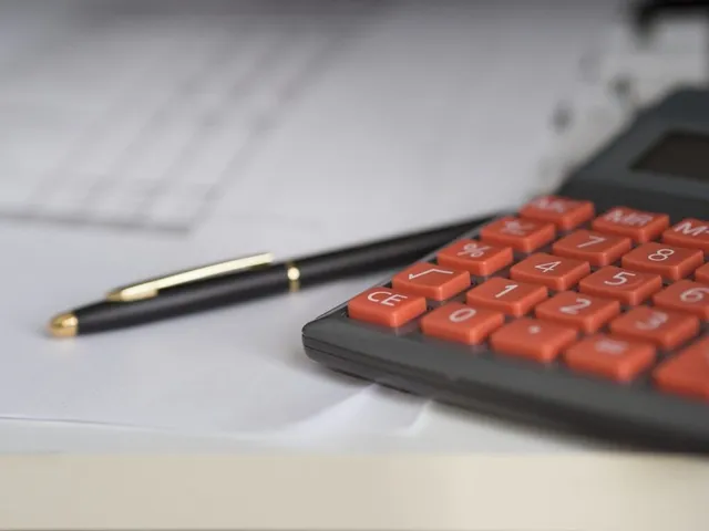 Un calculator cu taste portocalii și un pix negru cu detalii aurii sunt așezate pe hârtii albe.