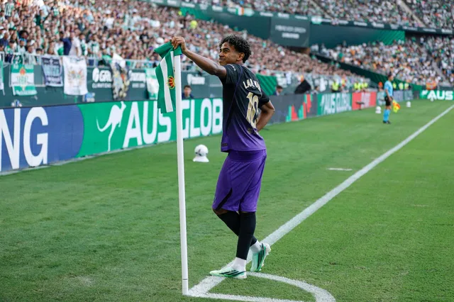 Un jucător de fotbal cu echipament violet și negru stă lângă stâlpul de colț al terenului pe o suprafață de gazon verde.