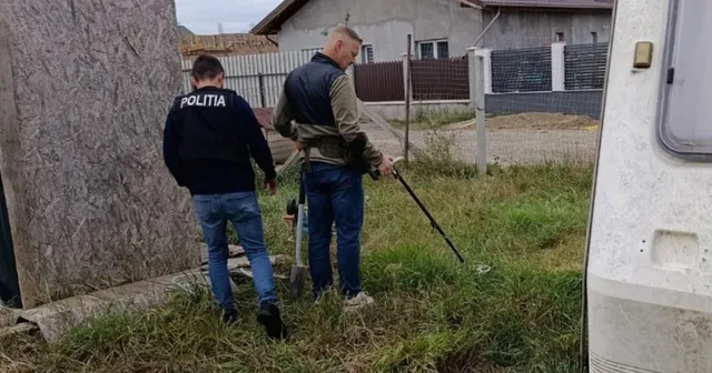Unii bărbați stau pe iarbă lângă un perete de beton și o mașină de camping, unul purtând un hanorac cu inscripția POLITIA.